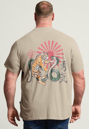 Mann trägt ein beiges Hemd mit Grafik eines kämpfenden Tigers und einer Schlange, roter aufgehender Sonne, Blume und japanischen Zeichen auf dem Rücken.