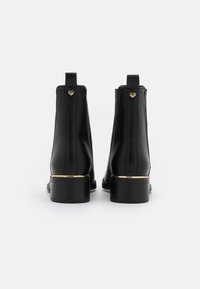 Czarne skórzane botki za kostkę z złotym akcentem na obcasie i małym serduszkiem na pętelce, charakteryzujące się gładkim wykończeniem i zarysowaną konstrukcją.