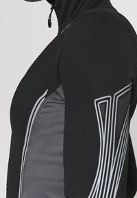 Black athletic long-sleeve top featuring a high collar, grey side panels, and reflective accents for visibility. Smooth texture.