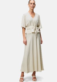 Lichtbeige jurk met zwarte diagonale strepen, wikkelontwerp, korte mouwen, een strik in de taille, vloeiende rok, gladde textuur.