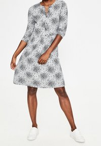 Szara sukienka z wzorem w czarne kropki, z rękawami do trzy czwarte i okrągłym dekoltem, zestawiona z białymi sneakerami.