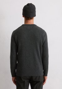Ciemnoszara wełniana sweter z prążkowanym dekoldem i mankietami, z teksturowanym splotem. Noszony z dopasowaną, ciemnoskalowanym beanie.