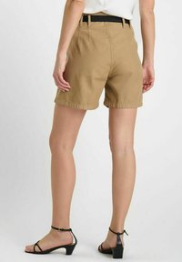 Shorts kaki à coupe droite, avec une taille noire et des coutures visibles. Portés avec des sandales noires et une texture lisse.