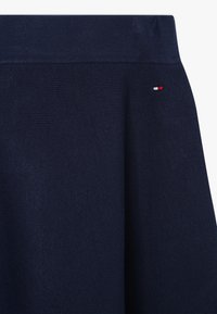 Marineblå strikket nederdel med en bred talje og et lille rød, hvidt og marineblåt flaglogo nær taljen på højre side.