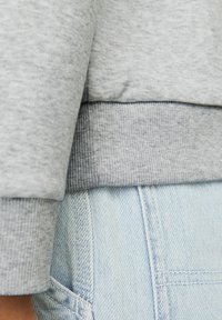 Tessuto grigio della felpa con bordo a coste sovrapposto a denim blu chiaro, in evidenza cuciture e dettagli di texture.