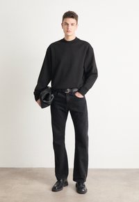 Felpa oversize nera, jeans di denim neri, cintura in pelle e scarpe nere. Texture liscia, design casual con una vestibilità rilassata.