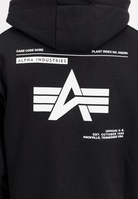 Zwarte hoodie met een grote witte grafische afbeelding, inclusief een hoekig logo en tekst, gemaakt van zacht katoen met een gladde textuur.