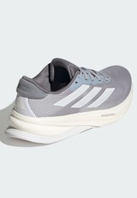 Chaussure de sport gris clair au design épuré, avec tige en mesh, accents blancs et semelle rembourrée. Présente une surface texturée et un talon renforcé.
