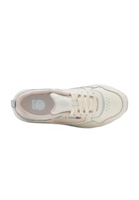 Zapatilla deportiva beige y blanca con cordones, puntera perforada, cuello acolchado y plantilla de malla con un logotipo de escudo.
