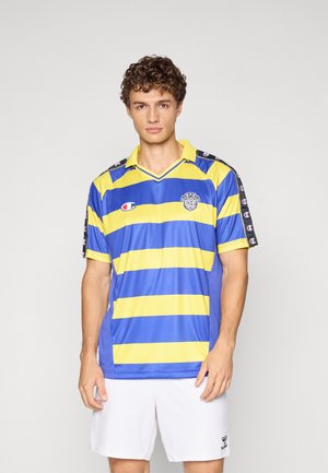 Man wearing blue and yellow horizontal striped sports jersey with white shorts, standing against a plain light background.