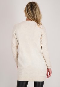 Lichtbeige lange mouw trui met een ronde hals, zachte textuur, ribgebreide manchetten en een rechte zoom, die tot halverwege de dij reikt.