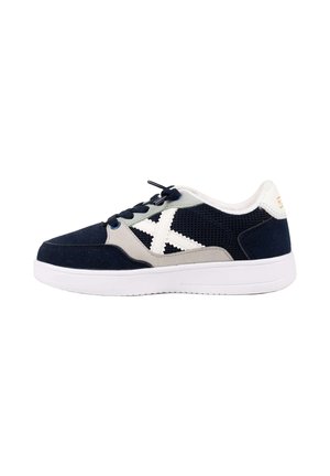 Zapatilla baja negra y gris con suela blanca, logo blanco "X" en el lateral de malla y cordones negros.