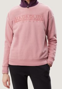 Felpa rosa con un design del logo testurizzato sulla parte anteriore, polsini e orlo a coste. Indossata sopra un top scuro, con una vestibilità comoda.