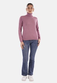 Maglione a collo alto di un delicato colore viola chiaro, con una vestibilità slim, realizzato in materiale morbido. Abbinato a jeans svasati blu scuro e sneaker bianche.