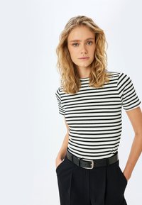 Camiseta de rayas en blanco y negro, con mangas cortas y de canalé, combinada con pantalones negros de cintura alta y un cinturón negro con hebilla plateada.