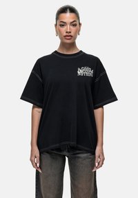 Czarna, oversize koszulka z krótkim rękawem, z białym graficznym napisem "GOOD FOR NOTHING" z przodu oraz kontrastującymi szwami.