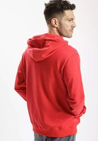 Czerwona bluza z kapturem o miękkiej fakturze, casualowym designie i ściągaczami na rękawach. Posiada kieszeń kangurzą oraz średniej długości dół z tyłu.