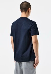Navy blue cotton T-shirt with short sleeves, featuring a round neckline and a side split at the hem, viewed from the back.