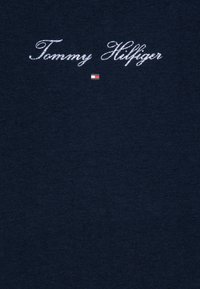 Tamno plava pamučna majica s bijelim vezom "Tommy Hilfiger" logotipa i malim logotipom u bojama ispod. Glatka tekstura, regularni kroj.