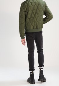 Kurtka bomberka w oliwkowo-zielonym kolorze, pikowana, z prążkowanym wykończeniem na dole, zestawiona z czarnymi jeansami i botkami do kostki. Na kurtce widoczny charakterystyczny wzór przeszyć.