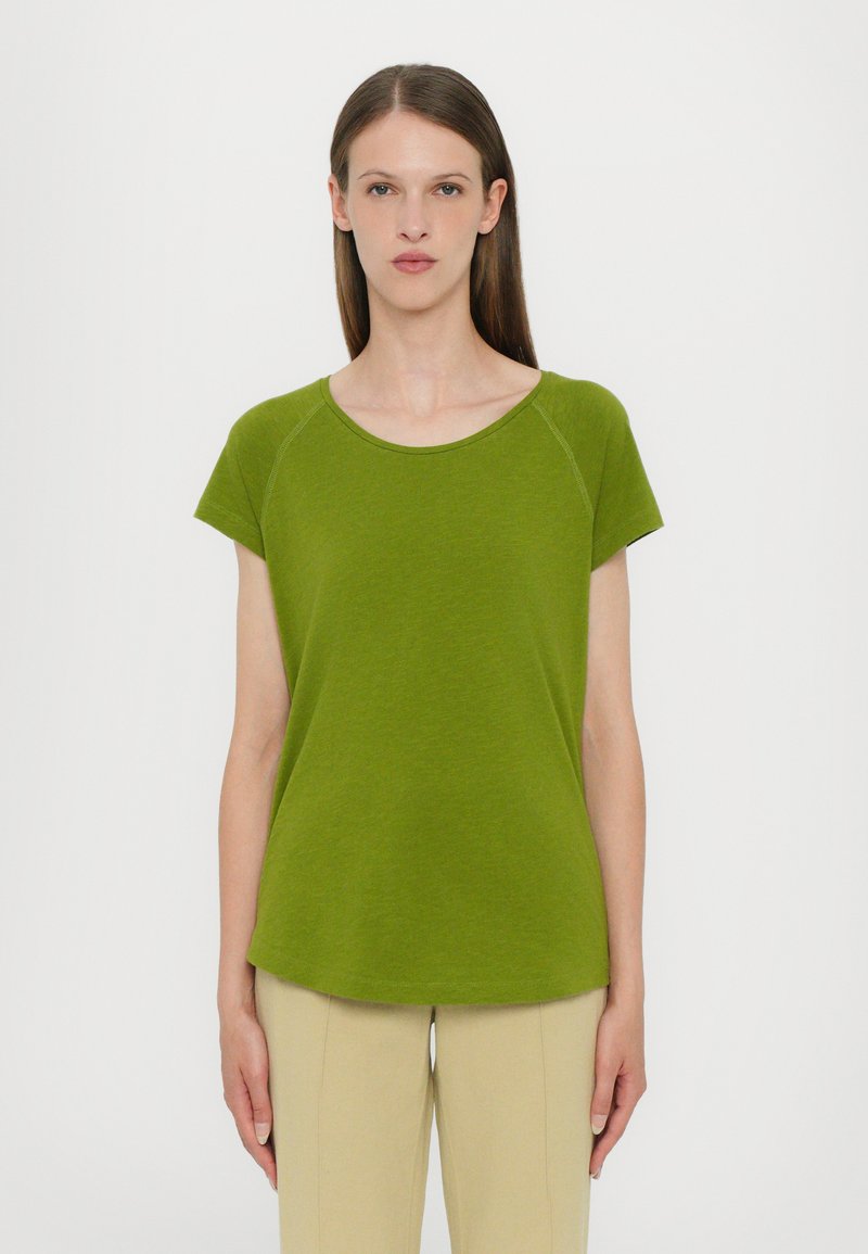 Green short-sleeve t-shirt with a round neckline, soft texture, and relaxed fit. Paired with cream-colored pants.