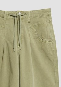 Pantalon vert clair avec poches avant, passants de ceinture, fermeture par boutons et cordon en tissu noué à la taille.