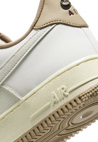 Gros plan sur le talon d'une basket blanche et beige montrant une semelle texturée avec "AIR" embossé et une partie du logo sur le panneau arrière supérieur.