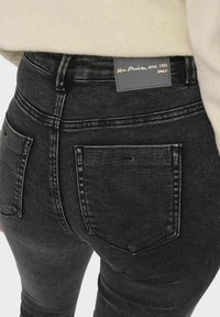 Svarta denimjeans med en skräddarsydd silhuett, utrustade med två bakfickor och en etikett med "Blue Denim anno 1995" i gyllene bokstäver.