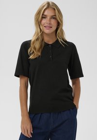 Camisa polo negra de manga corta, con cuello y tapeta de tres botones. Con dobladillo acanalado en la parte inferior. Textura suave.