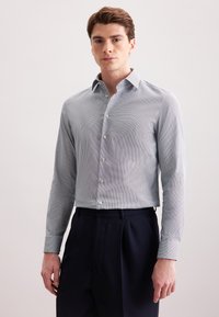 Camicia a maniche lunghe di colore blu chiaro con motivo, colletto button-down e una sottile texture. Indossata con pantaloni navy a vita alta.