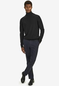 Musta pyörökaula-aukko neule yhdistettynä laivastonsinisiin housuihin ja mustiin kenkiin. Slim fit -malli, jossa on sileä pinta ja minimalistinen muotoilu.