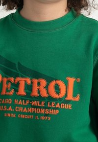 Grön sweatshirt med orange text "PETROL" och mindre text som hänvisar till Chicago Half-Mile League, U.S.A. Championship och 1973 års circuit.
