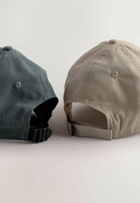 Kaksi lakkia aseteltu vierekkäin. Toinen on tummanharmaa, jossa on teksturoitu kangas, ja toinen on vaaleanbeige, jossa on sileä pinta. Molemmissa on säätöremmit takana.