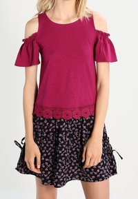 Top magenta con hombros descubiertos, mangas con volantes y detalle de encaje floral, combinado con una falda negra con un patrón floral rosa.