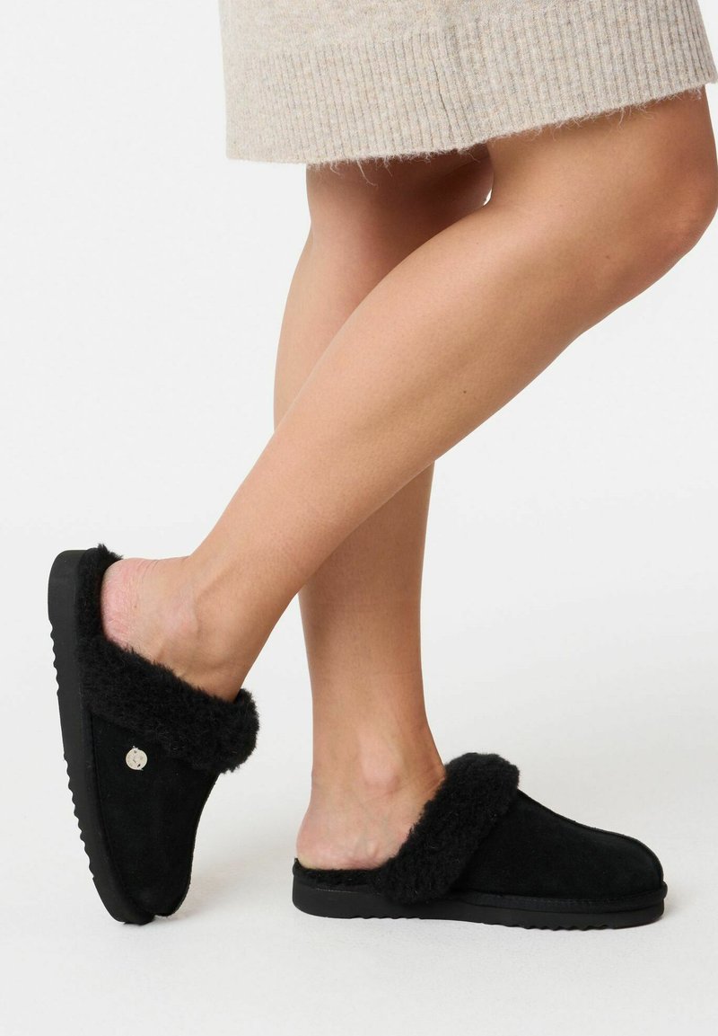 Sorte slip-on tøfler lavet af ruskind med en fluffy pelskrave. Tekstureret sål for godt greb. Simpelt design, ingen synlige mønstre eller accenter.