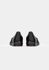 Black patent leather shoes with a smooth finish, low heel, and contrasting brown sole. Features rounded toe and lacing detail.