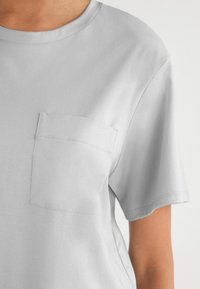 Szary t-shirt z krótkim rękawem, okrągłym dekoltem i kieszonką na piersi. Miękki, gładki materiał z dyskretnymi detalami szycia.