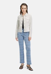 Veste en denim blanc avec des boutons pression, accompagnée d'un pantalon bleu à motifs présentant un design ikat. Des talons noirs à lanières complètent le look.