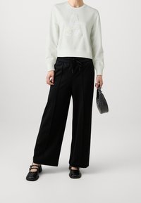 Světle šedá mikina s texturovaným designem "A", spárovaná s volnými černými kalhotami s elastickým pasem a černými botami na blokovém podpatku.