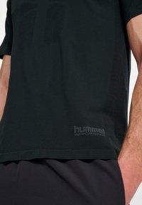 Zwart sport T-shirt met korte mouwen, voorzien van textuuraccenten en een prominent logo in een donkerdere tint. Gemaakt van ademend materiaal.