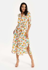 Floral midi dress with a button-down front, belted waist, vibrant fruit pattern in orange and pink on a cream background, and side slits.