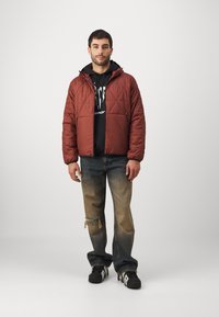 Padded red jacket with a quilted design and black hoodie underneath, paired with distressed blue jeans and black sneakers.