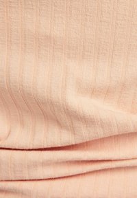 Łososiowy dzianinowy materiał w prążki z delikatnymi pionowymi paskami, miękką teksturą i subtelnym połyskiem, pokazujący fałdy i zagniecenia materiału.