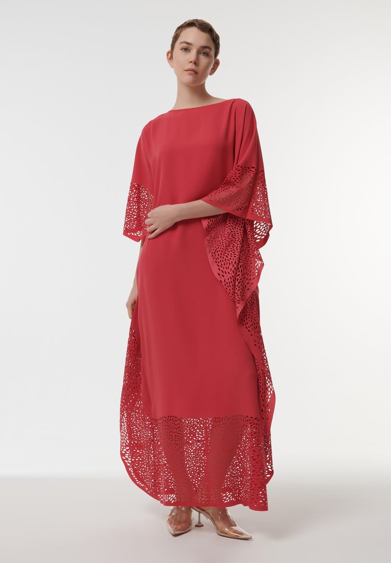 Rode maxidress met vleermuismouwen, voorzien van ingewikkelde lasergegoten kantdetails langs de randen. Vloeiende textuur, ontspannen pasvorm en een vloeiende silhouette.