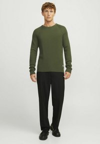 Olijfgroen geribbelde trui met een ronde hals, lange mouwen en een relaxte pasvorm, gecombineerd met zwarte wijde broek en zwarte schoenen.