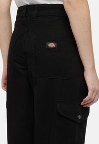 Zwarte werkbroek van stevig katoen, hoge taille, meerdere zakken en een geweven Dickies-logo patch op de achterkant.
