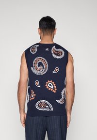 Tamsiai mėlynas megztinis liemenė su paisley raštais balta ir oranžine spalvomis. Rankovių neturinti, su briaunuotu apykakle ir apačia, pagaminta iš tekstūruotos medžiagos.