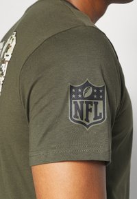 Olivgrön bomullströja med en stor NFL-logotyp och fem stjärnor på vänster ärm. Kort ärm och rundad halsringning.