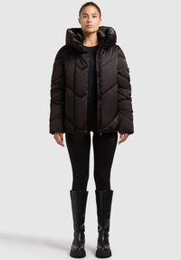 Black puffer jacket with a high hood, featuring a chevron pattern, front zipper, and a slightly cropped fit. Worn over a black top and leggings.