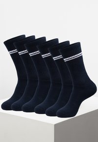 Marineblaue Baumwollsocken mit Rundstrick, gerippter Textur, mit weißen horizontalen Streifen nahe dem Bündchen. Sechs Paar in einer Verpackung auf einem hellen Podest präsentiert.